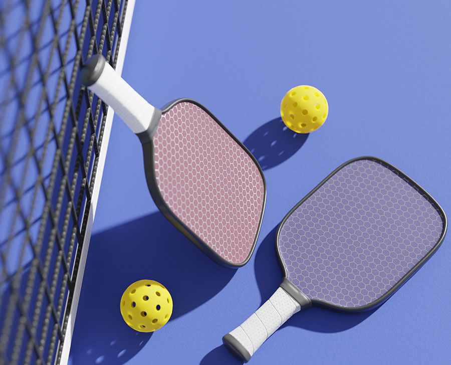 Two pickleball paddles and two yellow balls on a blue court near a black net.