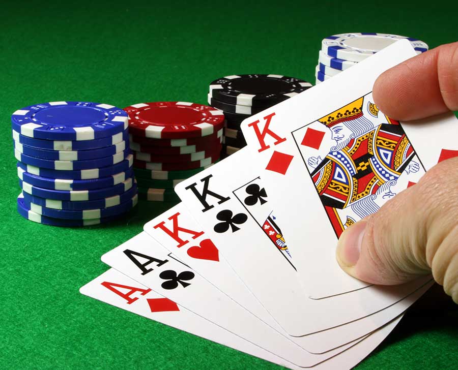 A hand holding four aces and a king with poker chips stacked on a green table.
